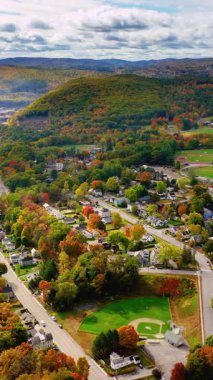Sonbahar ormanlarının ve tepelerdeki kasabaların havadan görünüşü. Beyzbol stadyumları ve küçük evleri olan sokaklar. Dikey video.