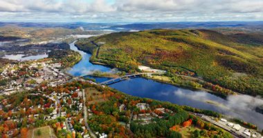 Geniş bir nehrin kıyısındaki resim gibi bir kasaba. Tepelerin ve sonbahar manzarasının havadan görünüşü. Amerika Birleşik Devletleri 'nin kuzeyi. Ufuktaki bulutlu gökyüzü.