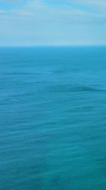 Küçük dalgalar ve açık mavi gökyüzü ile turkuaz okyanus suyunun sakin yüzeyi. Hava görüntüsü. Dikey video.