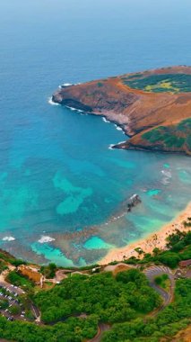 Resifli Hanauma Körfezi 'nin mavi suları. Sahilde kumlu plajları olan volkanik kraterlerin ve dinlenen insanların hava manzarası. Oahu Adası, Hawaii. Dikey video.