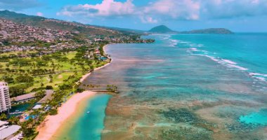 Pasifik sahil şeridine ulaşan turkuaz okyanus dalgasının havadan görüntüsü. Hawaii manzaralı güzel tropikal kumlu kumsal. Volkanların yamaçlarında bir şehir.