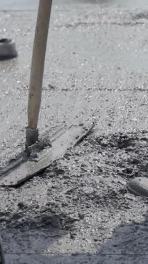 Yeni dökülmüş bir yüzeyde ıslak betonu pürüzsüz hale getiren bir el aletinin yakın çekimi. Alet ahşap bir sapa sahip ve malzemeyi düzleştirmek için kullanılır. Dikey video.