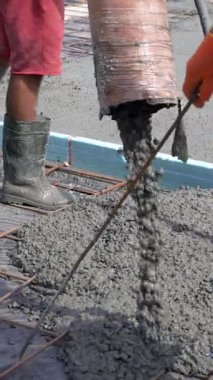 Beton, eldivenleri ve botları olan işçilerin rehberliğinde bir borudan demir parmaklıklara dökülüyor. Yüzey bir levha ya da temel oluşturmak için hazırlandı. Dikey video.