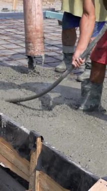 Özel bir cihaz kullanarak taze betonu titretiyor. İnşaat alanındaki çizmeli işçiler beton bir döşeme ve takviye ağ dökerler. Dikey video.