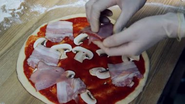 Şefin elleri bir parça et, bir dilim sosis ve domates ezmesi ve mantarlı bir pizzanın üzerine konur. Bir restoranda yemek hazırlamak için yakın plan..