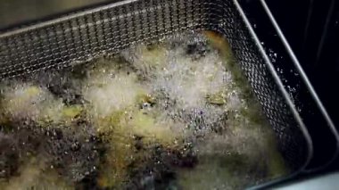 Patates kızartması kızartması kızartma makinesine dönüşüyor. Çıtır patatesler mutfakta kızgın yağda kızartılıyor. Mutfakta fast food hazırlama süreci. Üst görünüm, yavaş çekim.