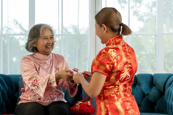 stock image Asian young woman give red bag to wish her mother and her mom give a lucky red envelope, They wearing Chinese traditional costumes sitting on sofa and smile with happy together