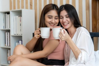 Asyalı genç ve güzel bir kadın yatakta sevgilisiyle birlikte sıcak kahve içiyor. Kadın aşığının romantik anı, LGBTQ aşk özgürlüğü kavramı, fotokopi alanı.