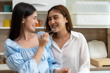 Asyalı genç ve güzel bir kadın ve kız arkadaşı mutfakta mutlulukla yemek yiyorlar. Kadın aşığın romantik zamanı, LGBTQ aşk özgürlüğü kavramı, kopyalama alanı.