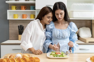 Asyalı genç ve güzel bir kadın ve kız arkadaşı mutfakta mutlulukla yemek yiyorlar. Kadın aşığın romantik zamanı, LGBTQ aşk özgürlüğü kavramı, kopyalama alanı.