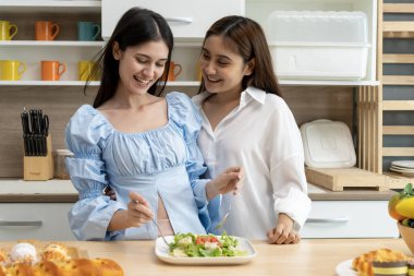 Asyalı genç ve güzel bir kadın ve kız arkadaşı mutfakta mutlulukla yemek yiyorlar. Kadın aşığın romantik zamanı, LGBTQ aşk özgürlüğü kavramı, kopyalama alanı.