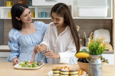 Asyalı genç ve güzel bir kadın ve kız arkadaşı mutfakta mutlulukla yemek yiyorlar. Kadın aşığın romantik zamanı, LGBTQ aşk özgürlüğü kavramı, kopyalama alanı.