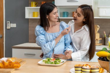 Asyalı genç ve güzel bir kadın ve kız arkadaşı mutfakta mutlulukla yemek yiyorlar. Kadın aşığın romantik zamanı, LGBTQ aşk özgürlüğü kavramı, kopyalama alanı.