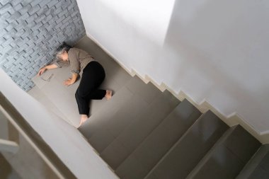 Gri saçlı kadın merdivenlerden düştükten sonra yerde baygın yatıyor..