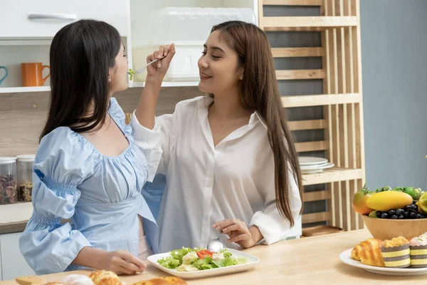 Asyalı genç ve güzel bir kadın ve kız arkadaşı mutfakta mutlulukla yemek yiyorlar. Kadın aşığın romantik zamanı, LGBTQ aşk özgürlüğü kavramı, kopyalama alanı.