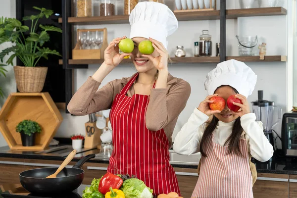 Mutlu güzel anne ve güzel kız mutfakta sağlıklı yemek hazırlıyorlar, elmayı komik bir şekilde yüzüne yerleştiriyorlar, uzayı kopyalıyorlar.