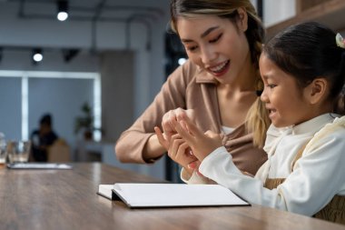 Güzel bir anne, güzel kızına evde ödev yapmayı öğretiyor. Konuşuyorlar ve gülüyorlar. Birlikte mutlu mesut.