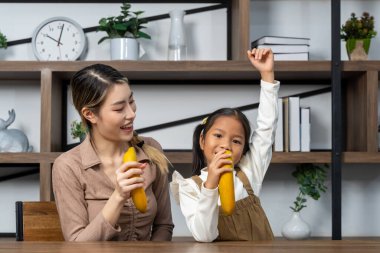 Asyalı genç anne ve onun küçük tatlı kızı evde eğlenceli aktif oyun zamanı geçiriyorlar. Onlar oturma odasında bir şarkı söylemek için muz kullandılar. Boşluğu kopyala