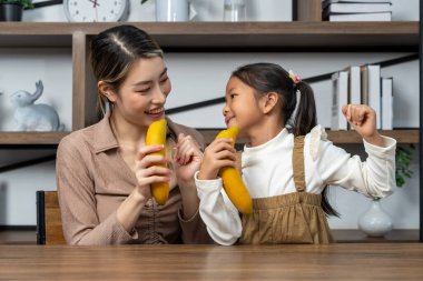 Asyalı genç anne ve onun küçük tatlı kızı evde eğlenceli aktif oyun zamanı geçiriyorlar. Onlar oturma odasında bir şarkı söylemek için muz kullandılar. Boşluğu kopyala