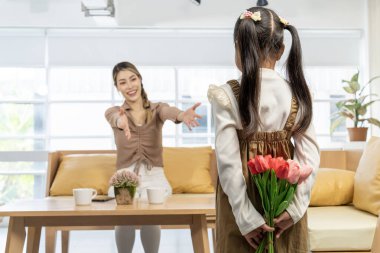 Anneyi selamlayan küçük güzel kızın arka manzarası ve evde bir buket çiçeğe lale vermesi. Anne ve kızı gülümsüyor. Mutlu aile tatilleri ve birlikteliğimiz. Anneler Günü konsepti.