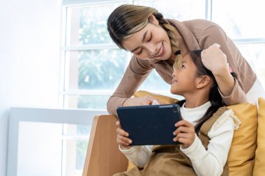 Asyalı genç anne ve güzel kız oturma odasındaki kanepede oturup tablet kullanıyor. Mutlu aile kavramı, kopyalama alanı.