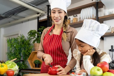 Mutlu anne ve güzel kız mutfakta sağlıklı yiyecekler hazırlıyorlar, anne kırmızı dolma biber kesiyor, mutlu bir şekilde konuşuyorlar, boşluğu kopyalayarak.