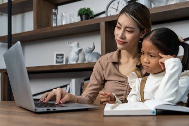 Güzel bir anne, güzel kızına evde dizüstü bilgisayarla ödev yapmayı öğretiyor. Oturma odasında konuşuyorlar ve mutlu bir şekilde gülümsüyorlar.