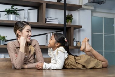 Asyalı genç anne ve onun küçük tatlı kızı evde eğlenceli aktif oyun zamanı geçiriyorlar. Şirin kız tahta masada uzanıp annesiyle oturma odasında konuşmaktan zevk alıyor. Boşluğu kopyala