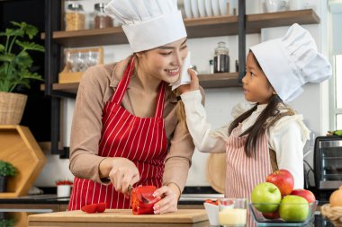 Mutlu anne ve güzel kız mutfakta sağlıklı yiyecekler hazırlıyorlar, anne kırmızı dolma biber kesiyor, mutlu bir şekilde konuşuyorlar, boşluğu kopyalayarak.