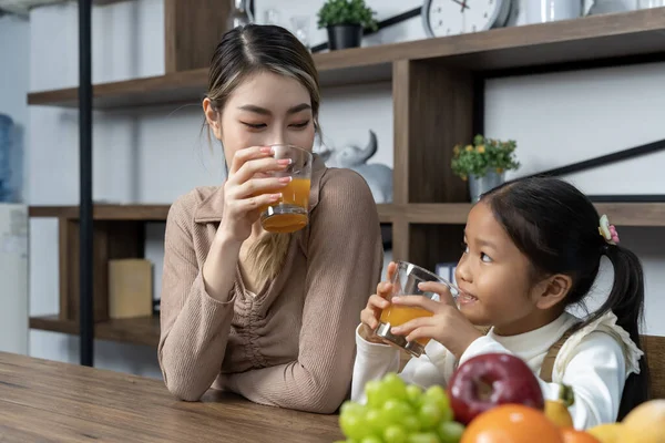 stock image Beautiful mother and her lovely daughter drink fresh orance juice on table in kitchen at house, they talking and smile with happy together, copy space