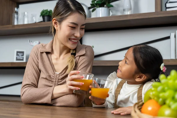 stock image Beautiful mother and her lovely daughter drink fresh orance juice on table in kitchen at house, they talking and smile with happy together, copy space