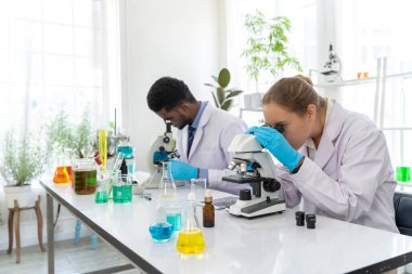 Mikroskop ve laboratuvar ekipmanlarıyla çalışan genç kadın bilim adamının portresi. Laboratuvarda yanında çalışan meslektaşı.