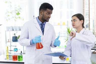 Genç bilim adamı ve bayan meslektaşı deney tüpünde sıvı deneyi yapıyorlar ve bilim laboratuarında çalışırken başparmağını kaldırıp işaret elini gösteriyorlar ve uzayı kopyalıyorlar.