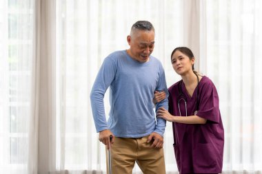 Asyalı fizyoterapist kadın ya da üniformalı özel hemşire huzurevindeki yaşlı bir adamın yürüyüşüne yardım ediyor. Fizik tedavi eğitiminde destek olarak baston kullanın, boşluğu kopyalayın