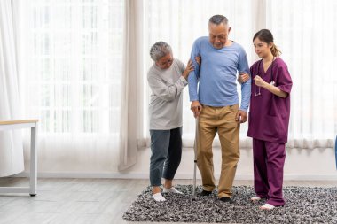 Üniformalı Asyalı fizyoterapist kadın ve huzurevindeki yaşlı bir adamın yürüyüşüne yardım eden yaşlı kadın. Fizik tedavi eğitiminde destek olarak baston kullanın, boşluğu kopyalayın