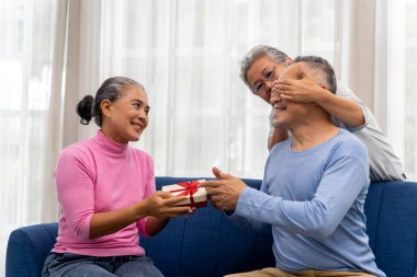 Asya 'lı kıdemli yaşlı bir kadın doğum günü hediyesi olarak hediye kutusunu elinde tutan yaşlı bir adamla ablasının gözlerini kapatıyor. Oturma odasında birlikte gülümseyin ve gülün. Ailecek iyi vakit geçirin.