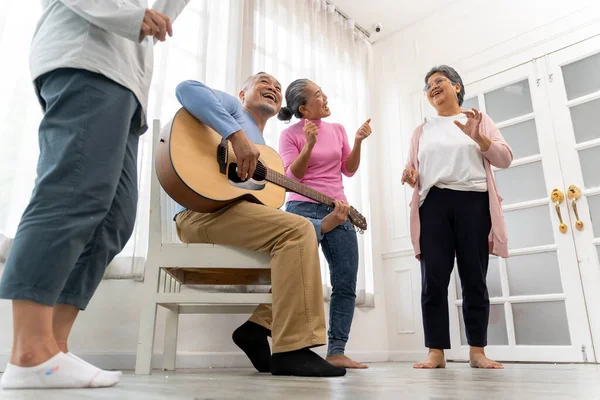 stock image Happy moment with Group of Asian senior man playing guitar and woman singing and dance with fun togetherness in living room at nursing home