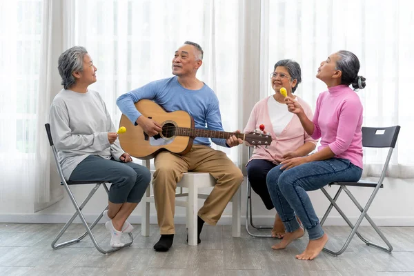 Happy moment with Group of Asian senior man playing guitar and woman singing and dance with fun togetherness in living room at nursing home