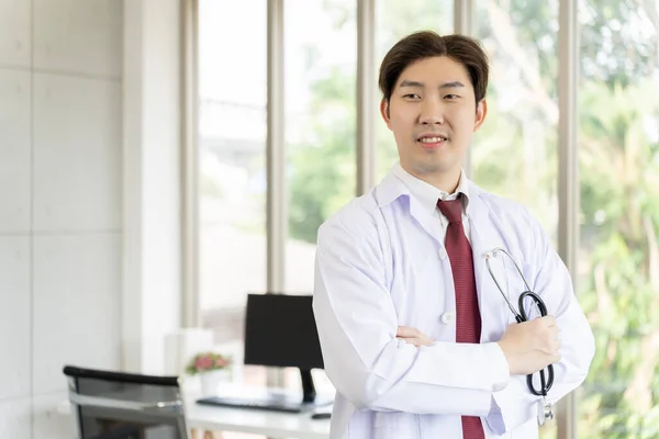 亚洲年轻男医生的画像 手持听诊器 双臂交叉 身穿白衣 微笑着远眺 复制空间 专业医生的概念 — 图库照片