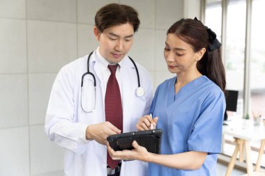 Beyaz üniformalı profesyonel doktor ve muayene odasında duran genç kadın cerrah hastanın sonuçlarını açıklamak için bir tablet kullanıyor. 