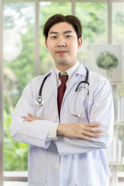 亚洲年轻男医生的画像 脖子上戴听诊器 双臂交叉 身穿白衣 笑着看着相机 专业医生的概念 — 图库照片