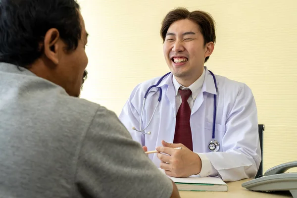 有选择地聚焦 身穿白衣的亚洲年轻男医生与男病人讨论治疗结果或症状 他们在一起笑着 — 图库照片