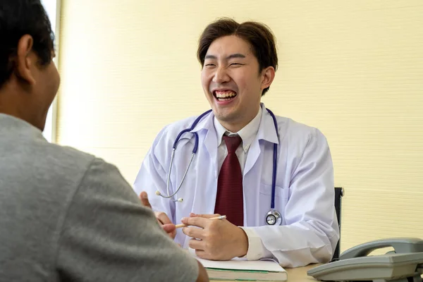 有选择地聚焦 身穿白衣的亚洲年轻男医生与男病人讨论治疗结果或症状 他们在一起笑着 — 图库照片