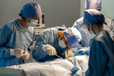 Ameliyathane ve tıbbi ekipmanların içinde kadın hasta cerrahi ekibinin yatağında ameliyata hazırlanıyor. Hasta güvenliği için iş sırasında birbirlerine danışıyorlar.