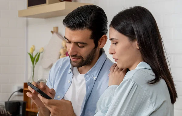 Portrait of Young couple using smartphone to sharing applications or checking social networks with happy together, Smiling married spouses playing online mobile games in kitchen at home