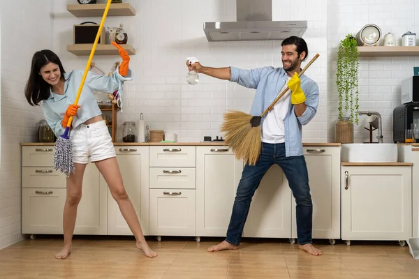 Young happy couple having fun while doing cleaning kitchen, They use broom and mop instead of musical instruments to enjoy dance together, Happy family concept
