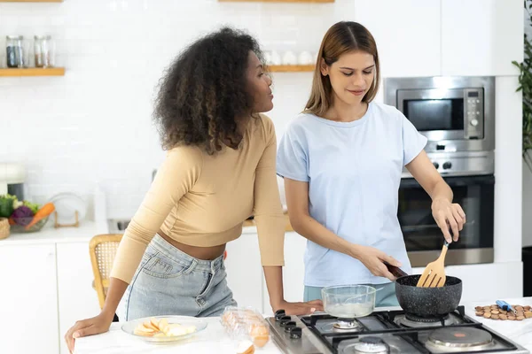 Two Woman is cooking in home kitchen. Young pretty woman standing preparing lunch in kitchen she holding pan with Healthy Food. Healthy Lifestyle. Cooking At Home.