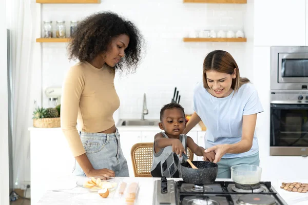 Two young women teach little children to cook in a modern kitchen. Young pretty woman and child standing preparing lunch in kitchen she making Healthy Food. Healthy Lifestyle. Cooking At Home.