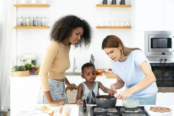Two young women teach little children to cook in a modern kitchen. Young pretty woman and child standing preparing lunch in kitchen she making Healthy Food. Healthy Lifestyle. Cooking At Home.