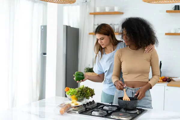 Two Woman is cooking in home kitchen. Young pretty woman standing preparing lunch in kitchen she holding pan with Healthy Food. Healthy Lifestyle. Cooking At Home.